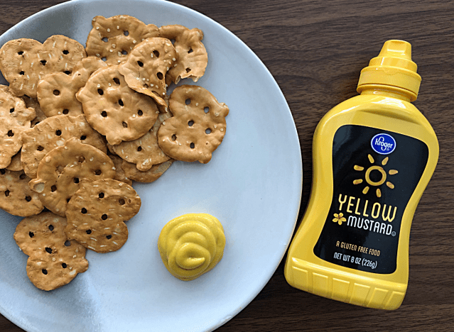 a bottle of kroger yellow mustard next to a plate of pretzels 