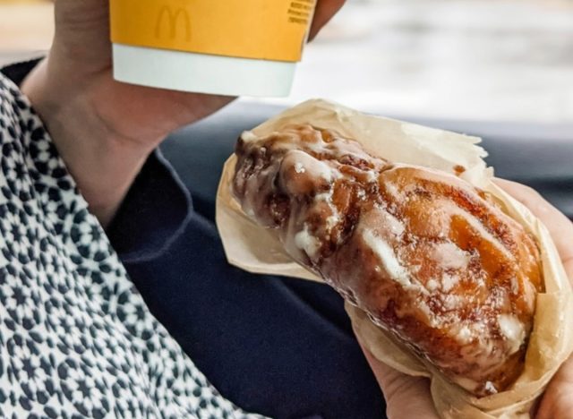 person holding mcdonald's apple fritter and coffee