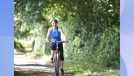 middle-aged woman riding bike outdoors on sunny day surrounded by foliage