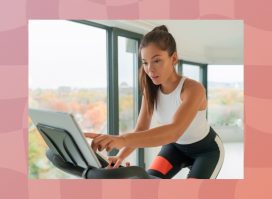 brunette woman on exercise bike in bright apartment surrounded by windows