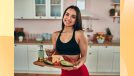happy fitness woman holding tray of healthy, protein-packed foods in bright kitchen