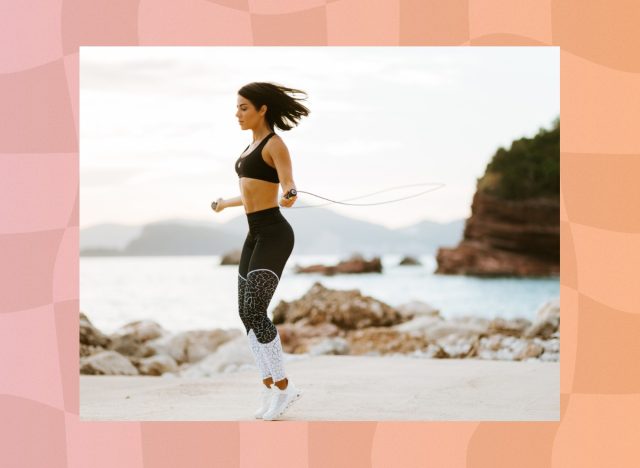 fit brunette woman in black sports bra and black and white leggings doing jump rope workout at the beach