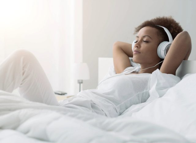 calm, peaceful woman listening to music in bed in bright room
