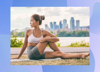 woman in sports bra and biker shorts stretching outdoors on yoga mat in front of city backdrop
