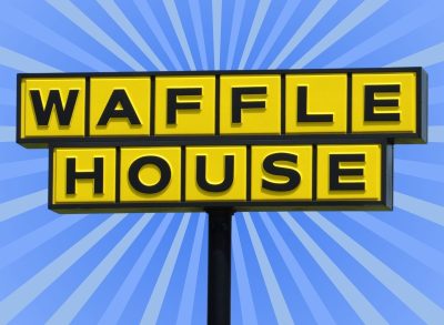 The iconic yellow sign f a Waffle House restaurant set against a vibrant blue background