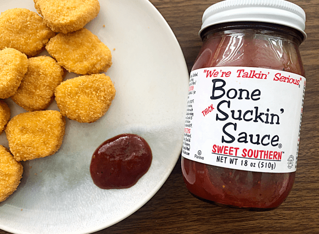 a jar of bone suckin bbq sauce next to a plate of chicken nuggets 