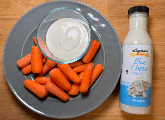a bottle of wegman's blue cheese next to a plate of carrots 