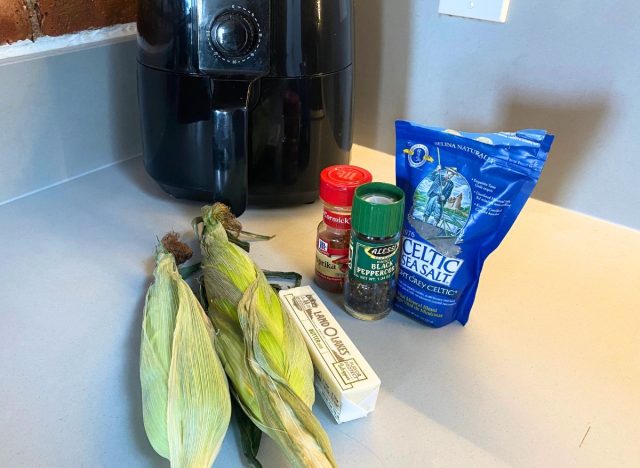 corn, butter and seasonings on a counter next to an air fryer