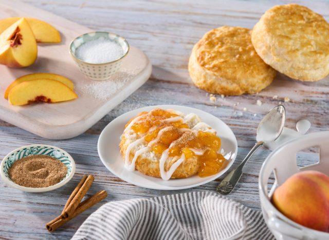 bojangles peach cobbler on a plate next to biscuits, peaches and small bowls of cinnamon and sugar