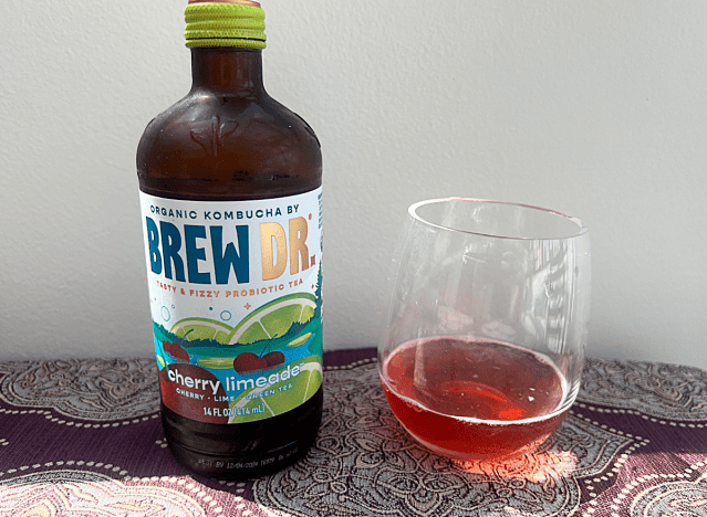 bottle of brew dr kombucha next to a glass of it 