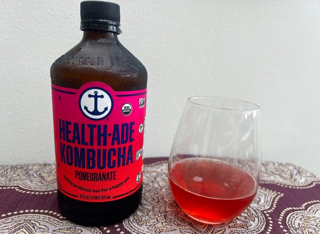 A bottle of Health-Ade Pomegranate Kombucha next to a small glass of the pink-colored beverage.