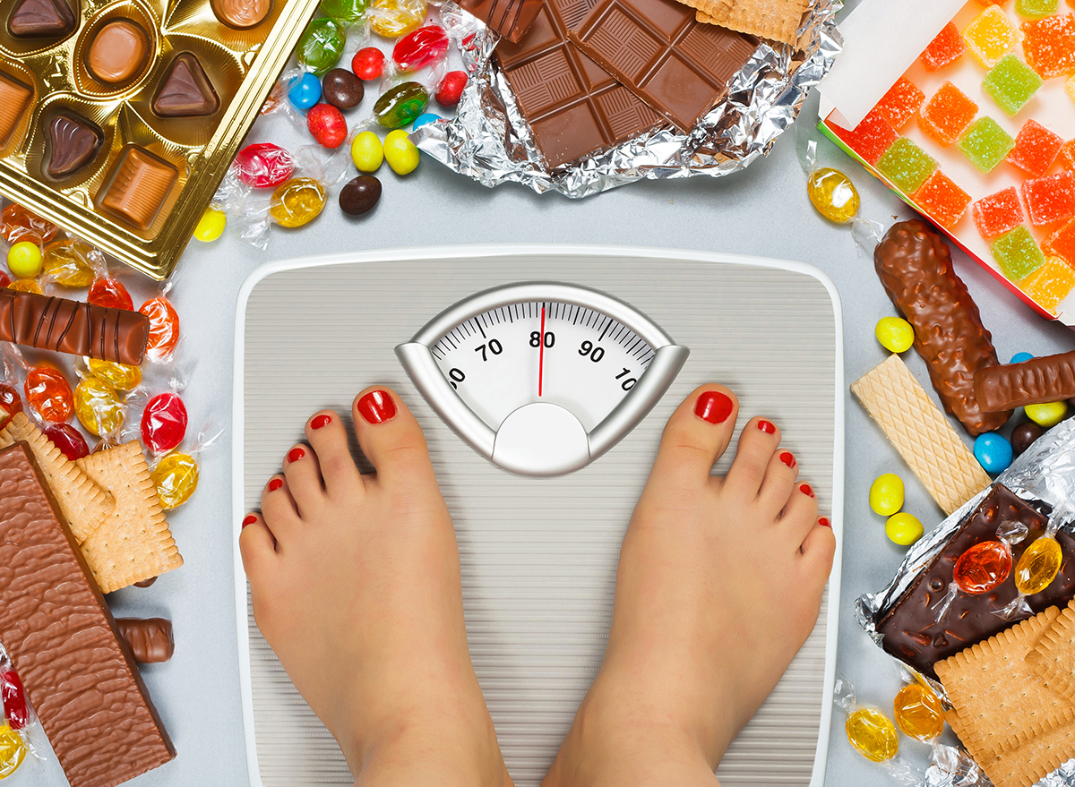Unhealthy diet - overweight. Feet on bathroom scale and chocolate, jelly cubes, candies, chocolate bars, cookies, donuts