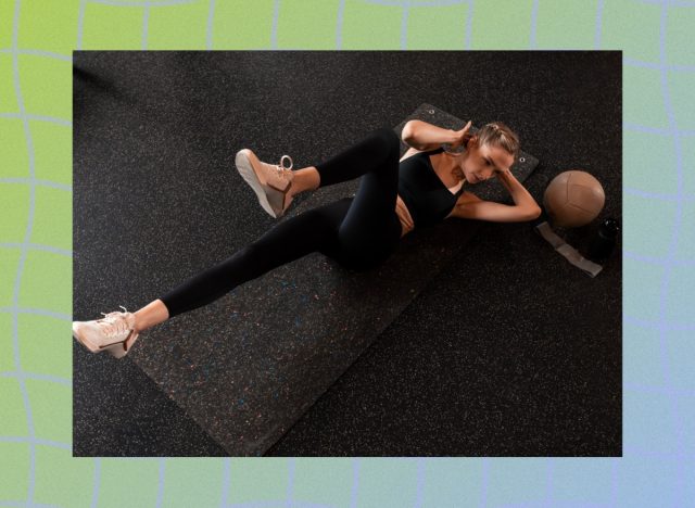 fit woman doing bicycle crunches on black yoga mat in dark gym setting