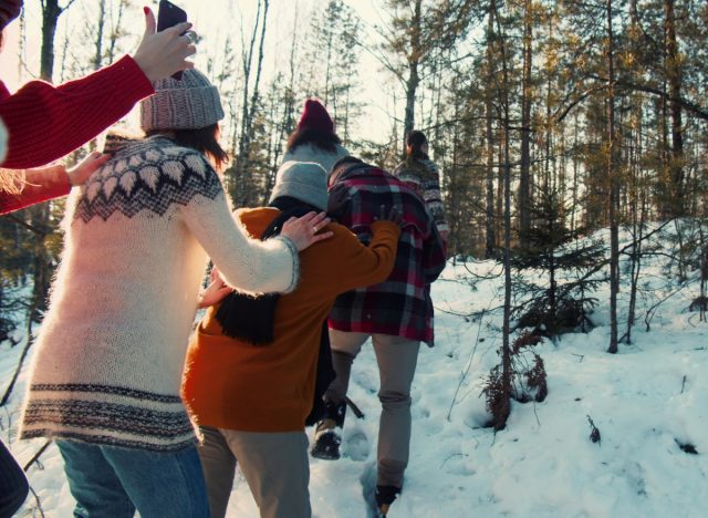 family in line taking a snowy walk on Christmas in sweaters and hats in the woods