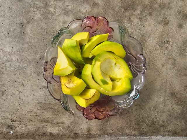 Sliced avocado in glass bowl on cement table from top view