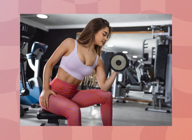 fit, focused brunette woman doing a dumbbell concentration curl at the gym
