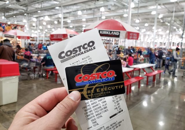 Montreal, Canada - October 26, 2019: A hand holding a receipt and Costco Executive Membership card in Costco warehouse. Costco is an American corporation which operates a chain of warehouses.