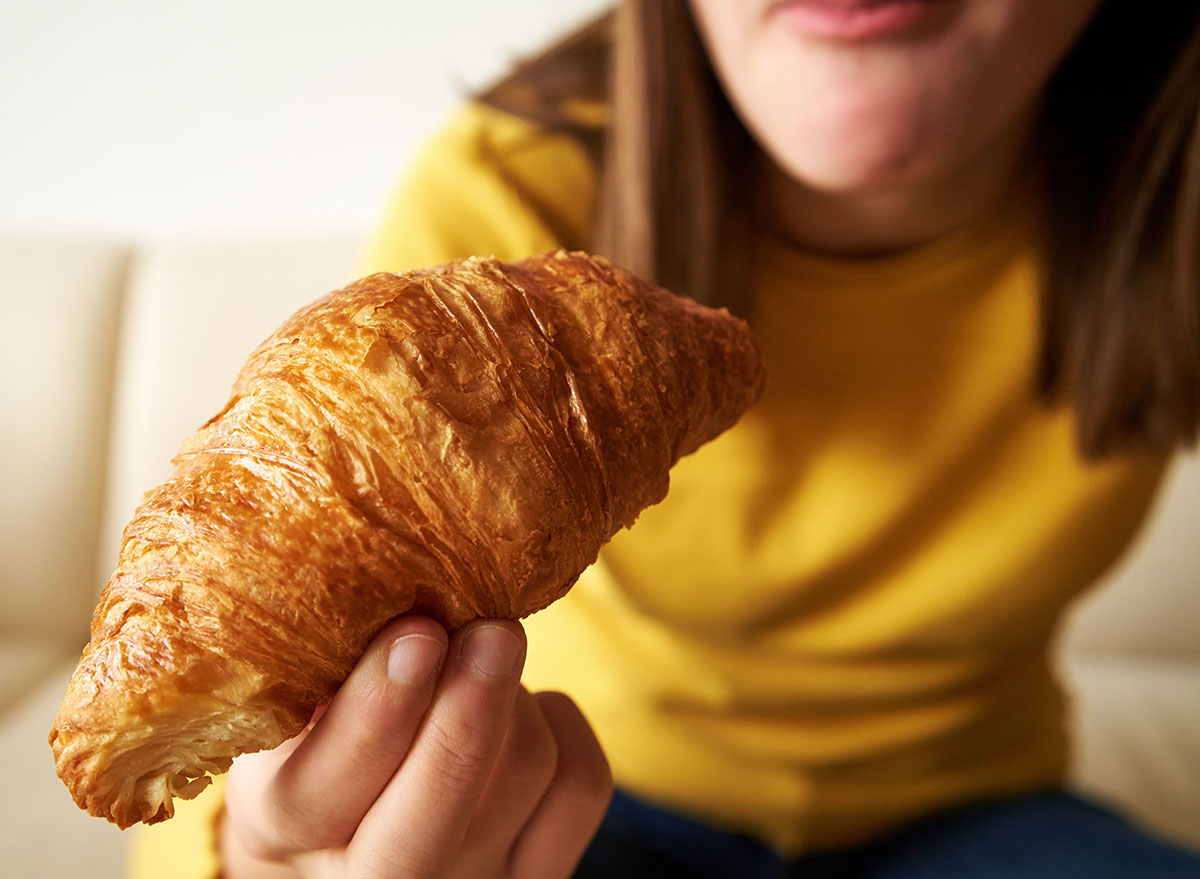 Teenage girl eating croissant for breakfast, close up
