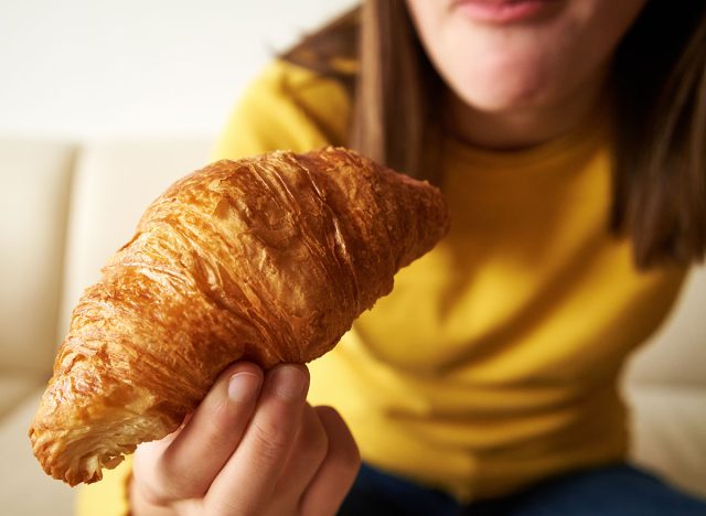 Teenage girl eating croissant for breakfast, close up