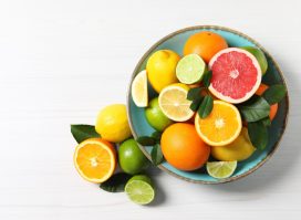 Different cut and whole citrus fruits on white wooden table, top view. Space for text
