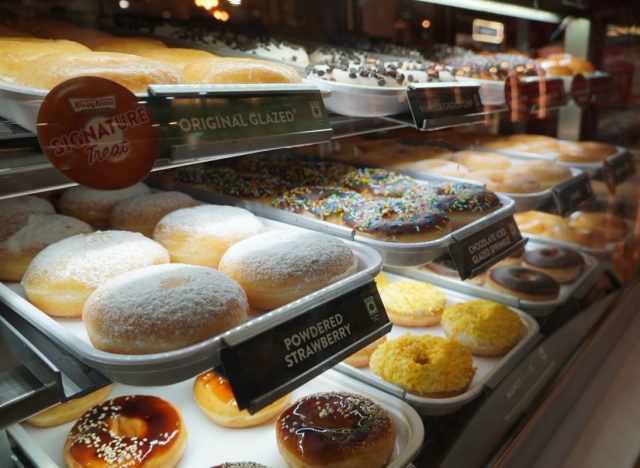 Display of delicious pastries with assorted glazed donuts in shop counter. Various donuts on shelf in Bakery. Colorful flavor donuts with coating, topping in glass showcase. Goa India - May 2021