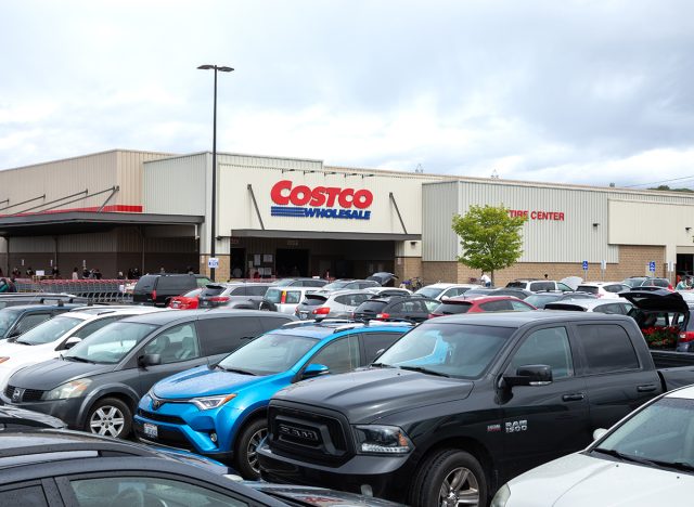 Full parking lot at a Costco Wholesale warehouse, with queue of shoppers in the distance