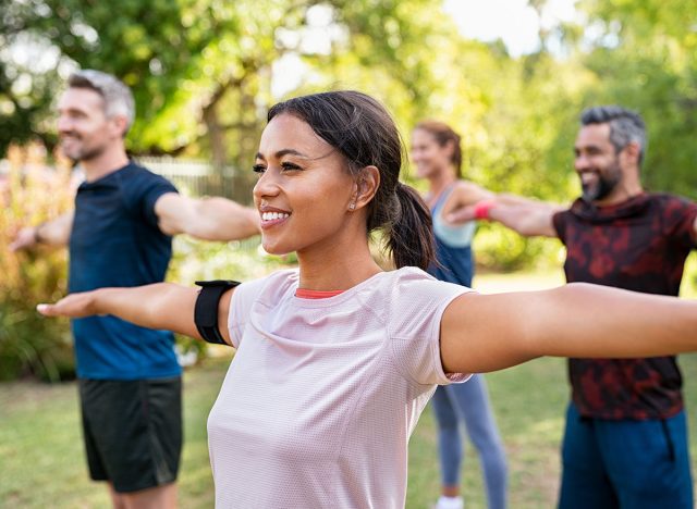 Group of multiethnic mature people stretching arms outdoor. Middle aged yoga class doing breathing exercise at park. Beautifil women and fit men doing breath exercise together with outstretched arms.