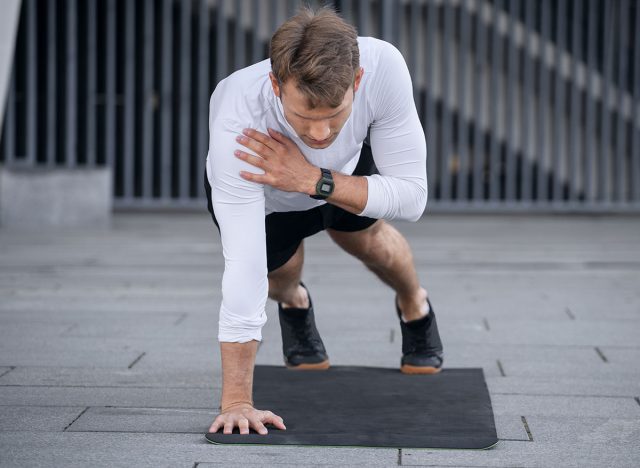 Full length view of young sportsman doing shoulder tap in push or press ups exercise, standing in plank position. Athlete with smartwatch training outdoors, warm up body, working out on yoga mat