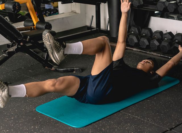 A young man doing a set of dead bug exercises lying on a mat. Leg and arm raised alternately. Abdominal and core workout at the gym.