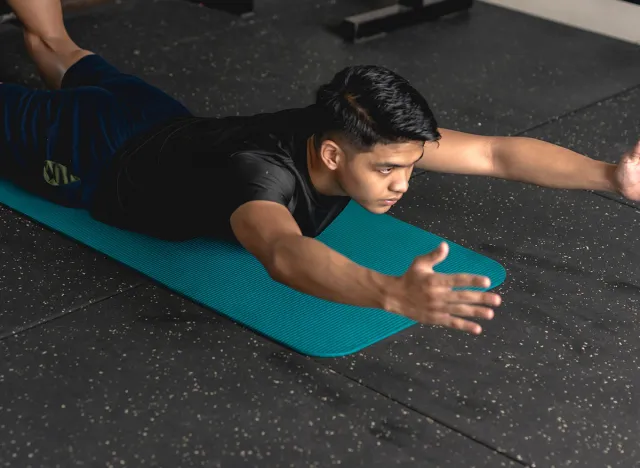 A young handsome asian man does superman back extension exercises while lying prone on a mat at the gym. Training and strengthening lower back muscles.