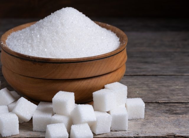 Granulated sugar in a wooden cup, a scattering of refined sugar cubes