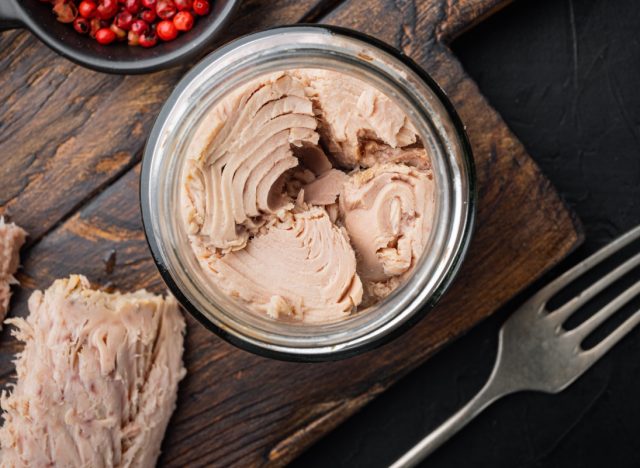 Canned tuna fillet meat in olive oil, on black background, flat lay