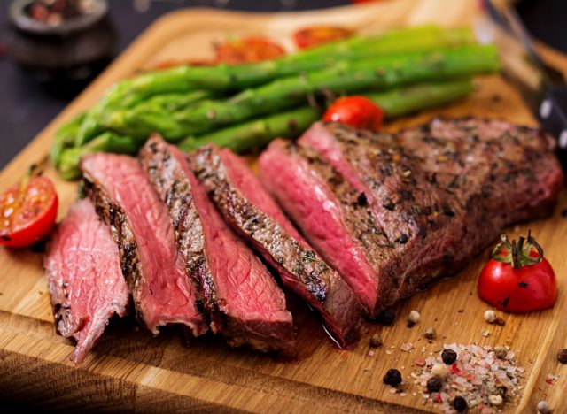Juicy steak rare beef with spices on a wooden board and garnish of asparagus.