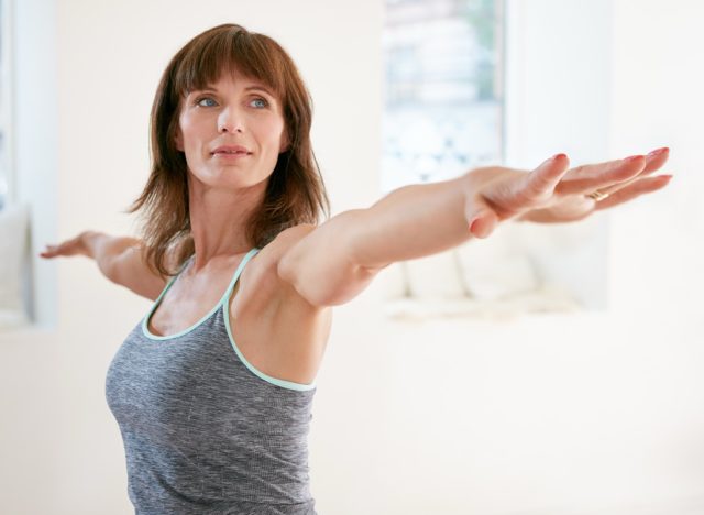 Portrait of mature woman stretching her arms and looking away at gym. Beautiful woman performing yoga in warrior pose, Virabhadrasana.
