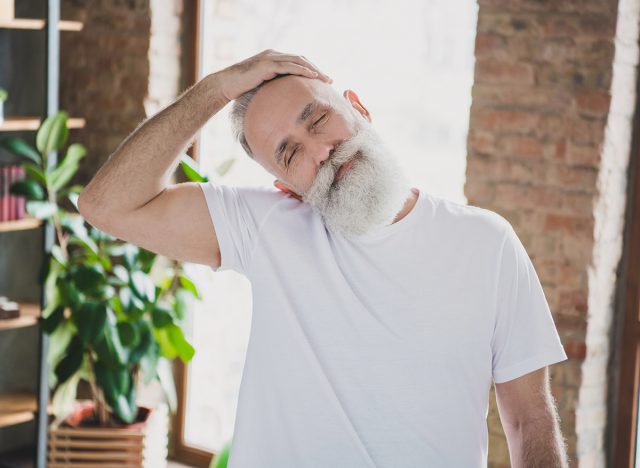 Mature man stretching neck with closed eyes exercising at home 