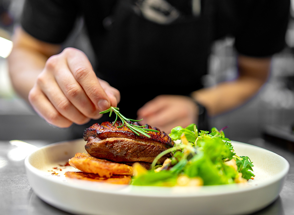 A skilled chef artfully garnishes a perfectly grilled steak with fresh herbs, elegantly plated on white porcelain