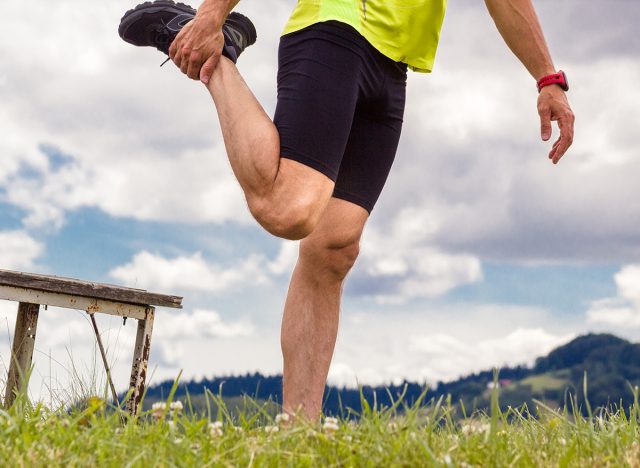 Male runner stretching outdoors at mountains background. Standing quadriceps quad stretch. Walking Heel to Butt.