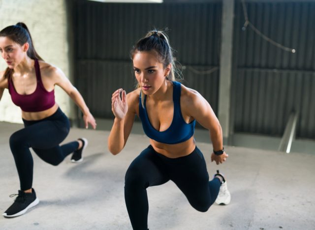 Athletic young woman with a healthy lifestyle doing leg lunges during a HIIT class. Women working out together at the fitness center
