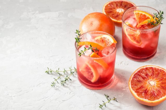 Red cocktail in base of Campari or bitter with Sicilian red oranges (tarocco) on light gray concrete background, copy space. Aperitif with Americano cocktail. Natural eco aesthetic, summer light
