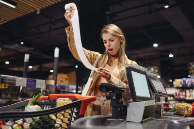Young sad customer woman wears casual clothes read bill at checkout shopping at supermaket store grocery shop buy with trolley cart choose products in hypermarket. Purchasing food gastronomy concept