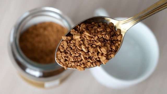 Close-up of a beautiful spoon filled with freeze-dried instant coffee above the coffee jar and an empty cup on the table