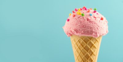Ice cream cone close-up. Pink Icecream scoop in waffle cone over blue background. Strawberry or raspberry flavor Sweet dessert decorated with colorful sprinkles, closeup