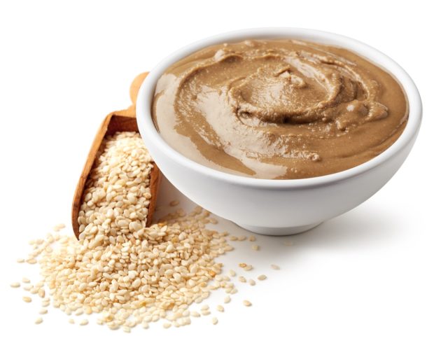 Bowl of tahini sauce and sesame seeds isolated on white background