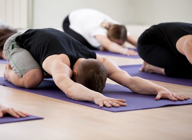 Group of young sporty people practicing yoga lesson, doing Child exercise, resting in Balasana pose, working out, indoor studio session close up, students training in club. Healthy wellbeing lifestyle