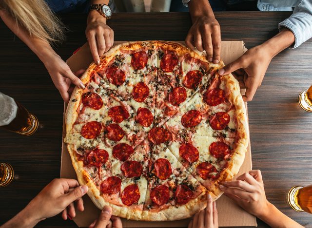 High angle shot of a group of unrecognizable people's hands each grabbing a slice of pizza