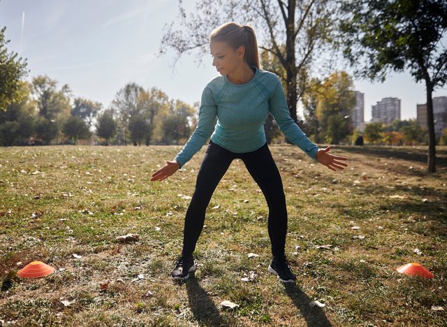 one young woman, 20-29 years old, cardio exercise in public park, between two fitness props, Lateral Shuffle, outdoors, sunny autumn day.