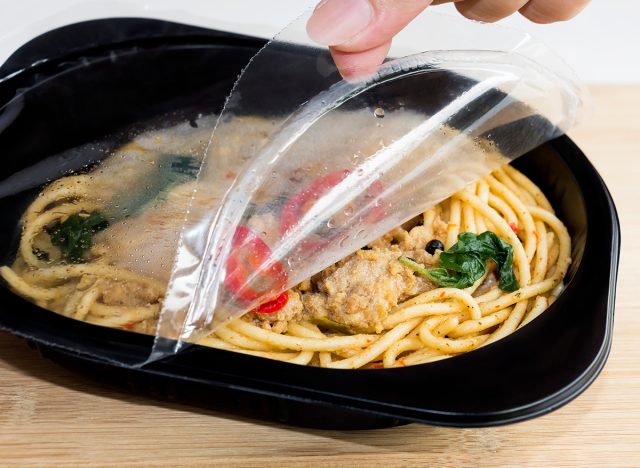 Food Delivery service: Woman hands holding open cling wrap and take out food in plastic boxes on wood background. concept online order take away food ready for home delivery.
