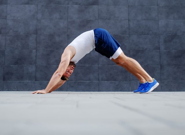 Side view of handsome fit muscular caucasian man doing inchworms exercise and looking at camera.