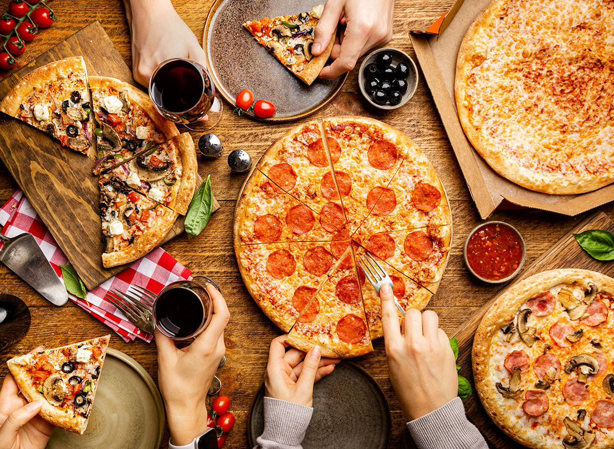 Family or friends pizza party. Flat-lay of people eating different types of pizza and drinking red wine over rustic wooden table, top view.
