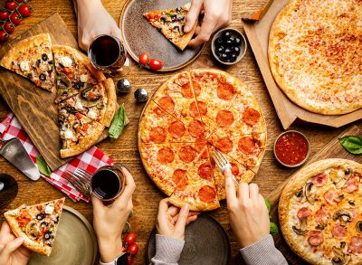 Family or friends pizza party. Flat-lay of people eating different types of pizza and drinking red wine over rustic wooden table, top view.